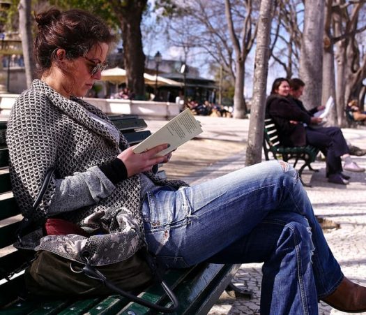 A photograph of a woman reading a book on a park bench.