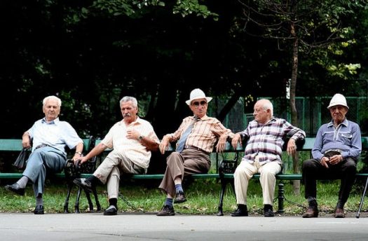 A photograph of 5 elderly men sitting on park benches.