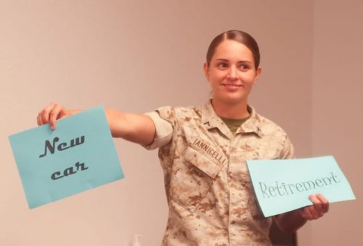 Service member holding one sign that says, "New car" and another that says, "Retirement"