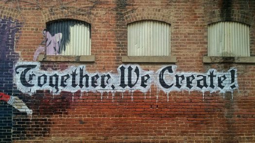 Brick wall with graffiti that says, "Together, We Create!"