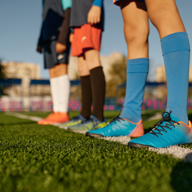 Closeup leg of teenage football player on white line across green soccer lawn with artificial grass