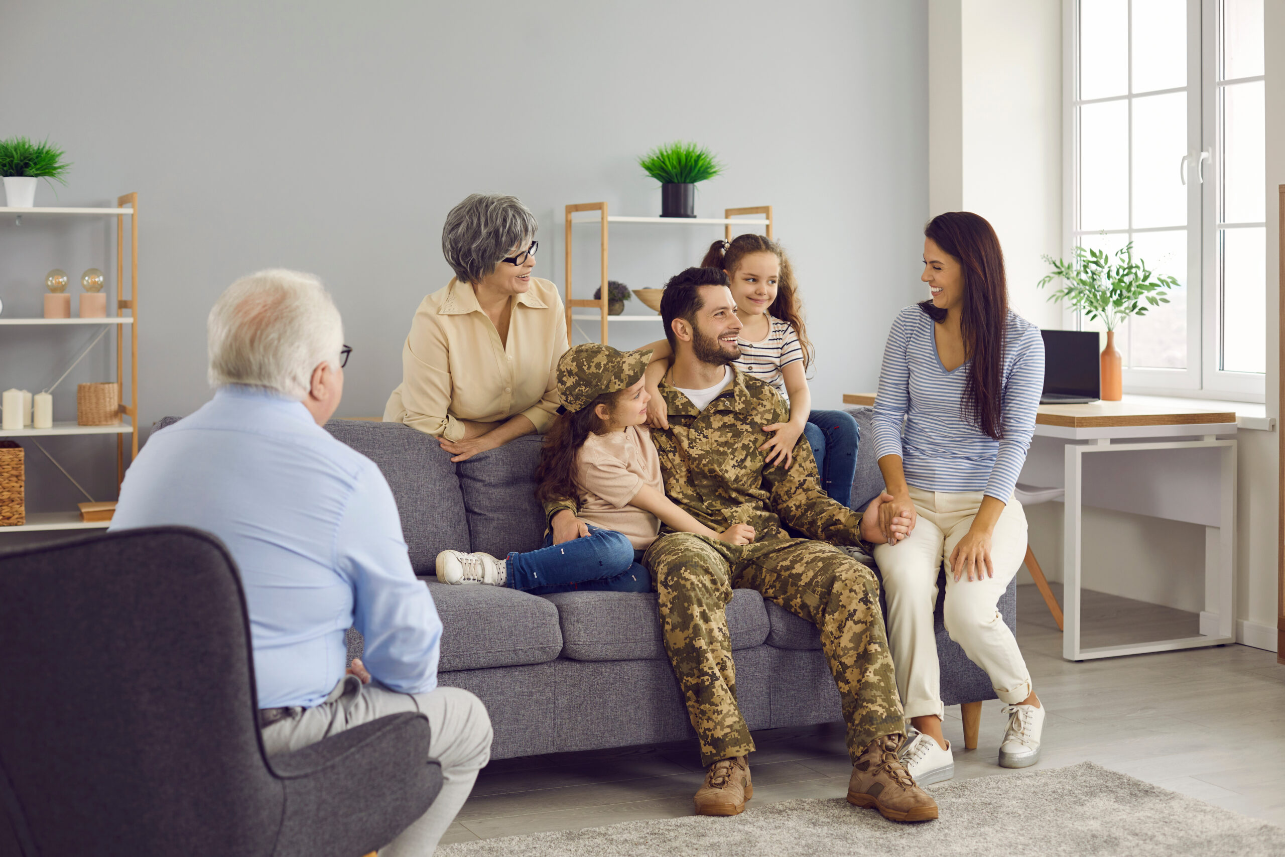 Returning to the family. Happy soldier man is talking with his family after returning from military service sitting in the living room at home. Older parents, wife and children all rejoice together.