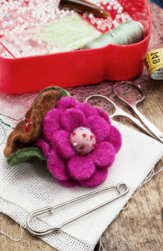 Felt flower next to safety pin, scissors, tape measures, and box of beads and thread
