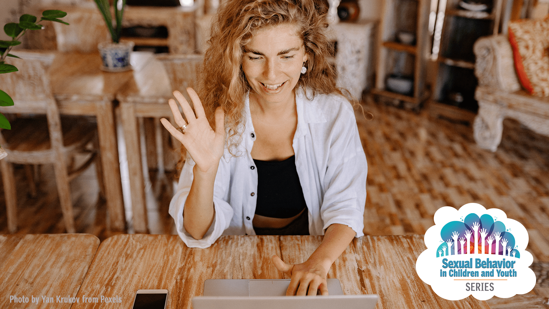 image of woman sitting at table on her laptop waving at webcam