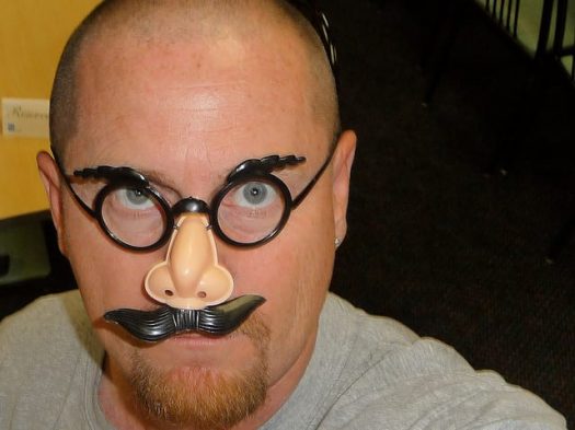 A photograph of a man wearing fake glasses, nose and mustache.