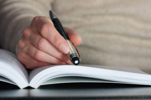 A photograph of a woman's hands holding a pen over a book.