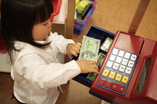 Child putting play money into a toy register