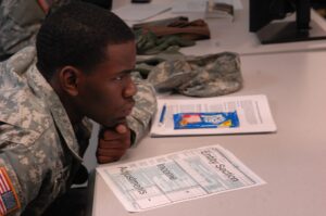 A photograph of a male solider sitting in a classroom at a desk with a tax form in front of him.