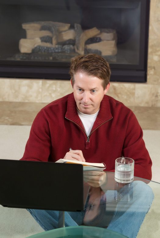 Man looking at laptop and taking notes