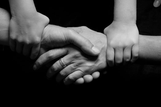 Two adult handings clasping with a child hand holding the wrist of each adult hand.