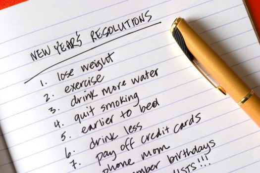 Notepad with New Year's Resolutions: 1. lose weight 2. exercise 3. drink more water 4. quite smoking 5. earlier to bed 6. drink less 7. pay off credit cards 8. phone mom 9. remember birthdays