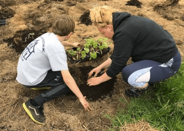 Young boy and adult volunteer collaborate on planting in a vegetable garden