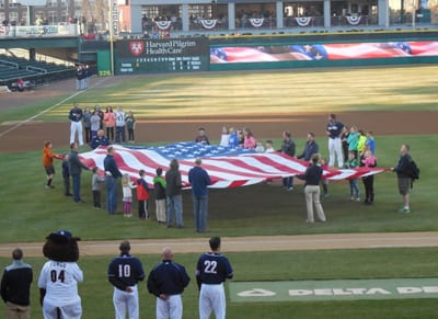 Youths and adults holding American flag on baseball field