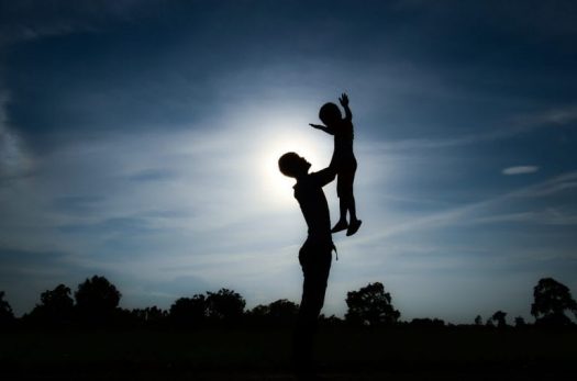 Silhouette of man holding young child in the air