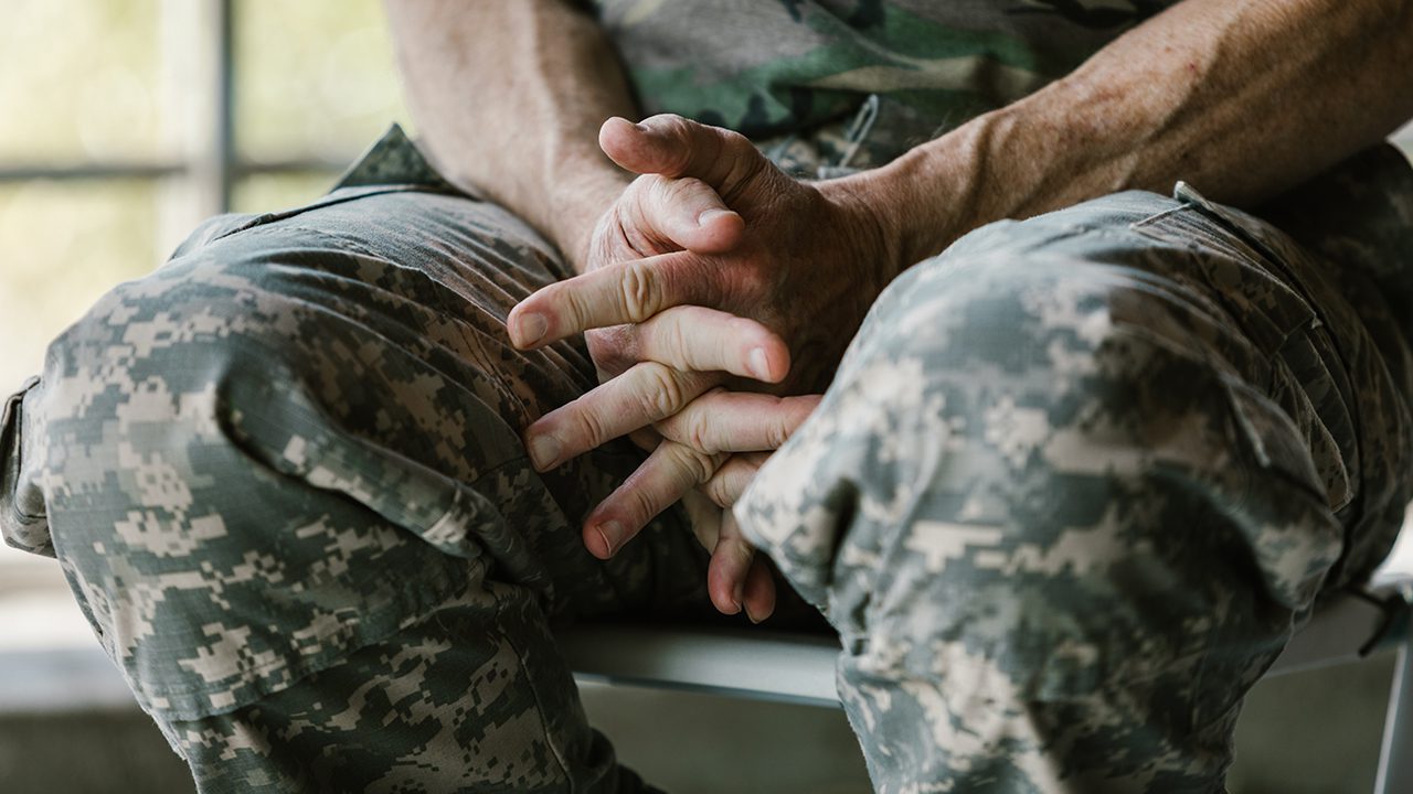 close up photo of man in a camouflage shirt sitting with his hands crossed