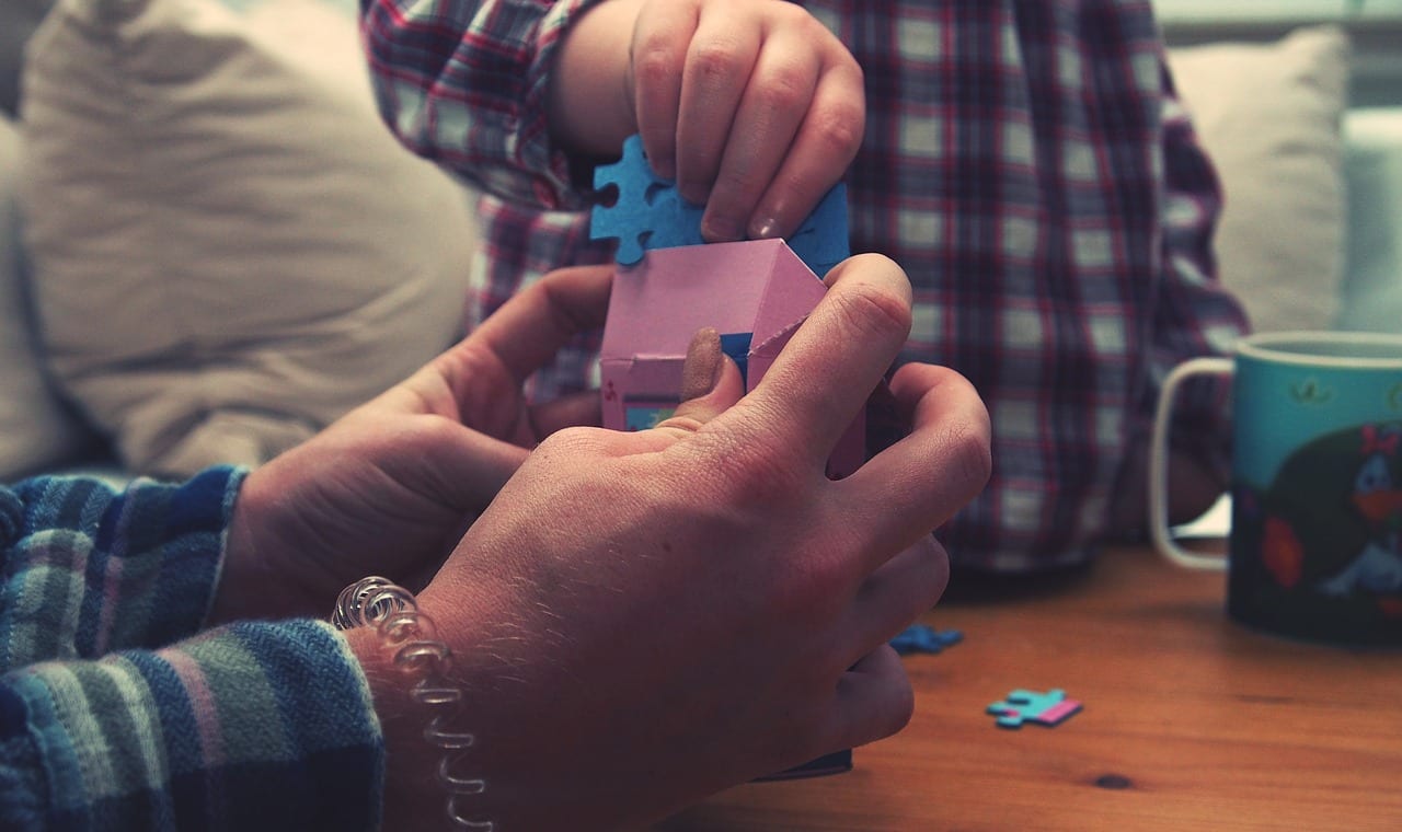 Hands of adult and hands of child holding puzzle pieces