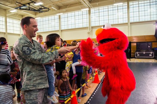 Elmo high-fiving a young girl as her father holds her