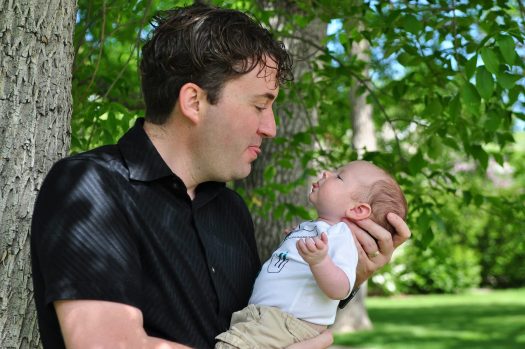 Father holding infant outside, both sticking out their tongues