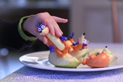 Child's hand holding toy over apple slices