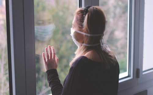 Woman looking out window with face mask on
