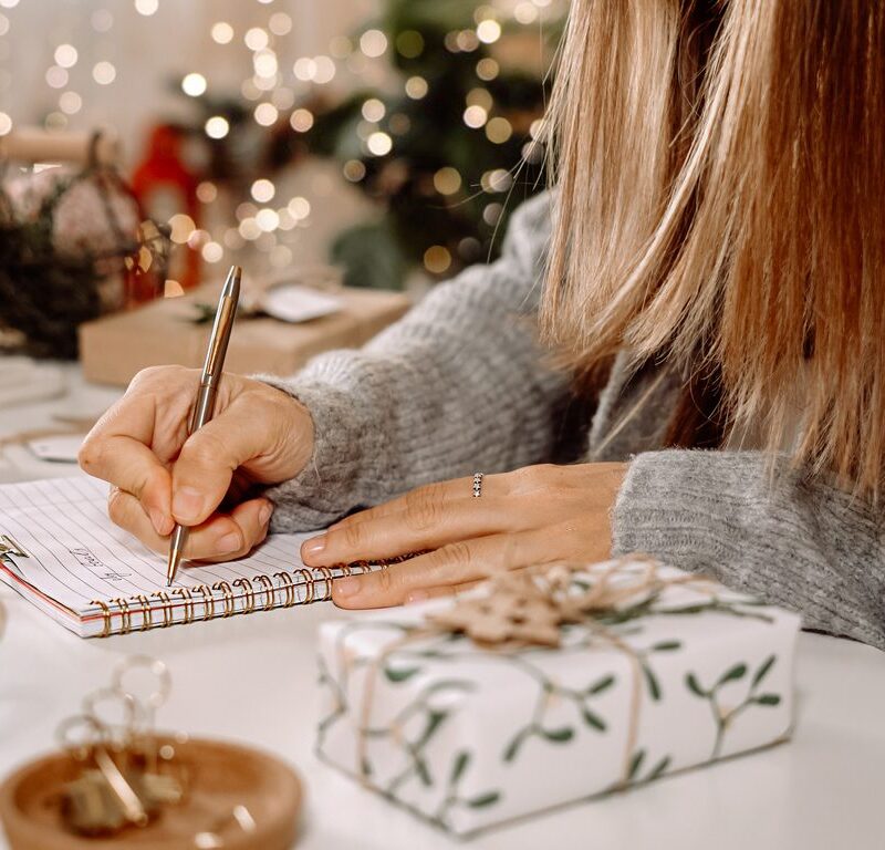 Goals plans make to do and wish list for new year christmas concept, girl writing in notebook. Woman hand holding pen on notepad at home on winter holidays xmas. Christmas decoration, gift boxes