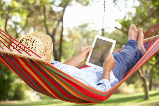 Man wearing hat relaxing in hammock with e-book