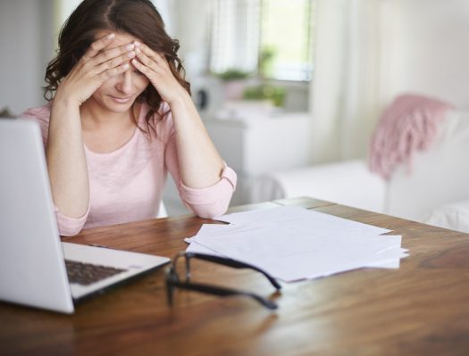 Woman holding her forehead as she looks at papers on desk