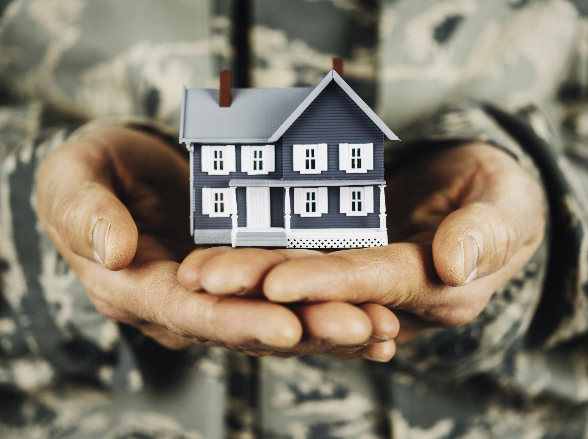 Close up of military service member holding a miniature house in their hands.