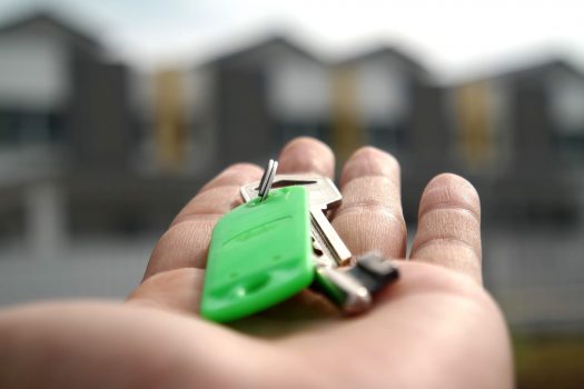 A photo of an outstretched hand holding a key ring with a green key chain and gold keys attached.