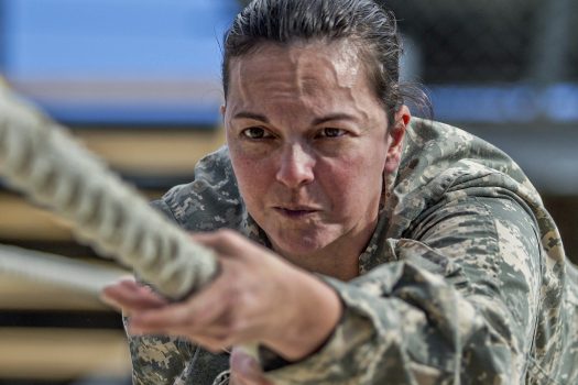 Female service member in uniform performs a rope pull during military training