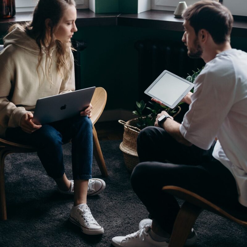 Woman holding laptop talking to a man holding a tablet.