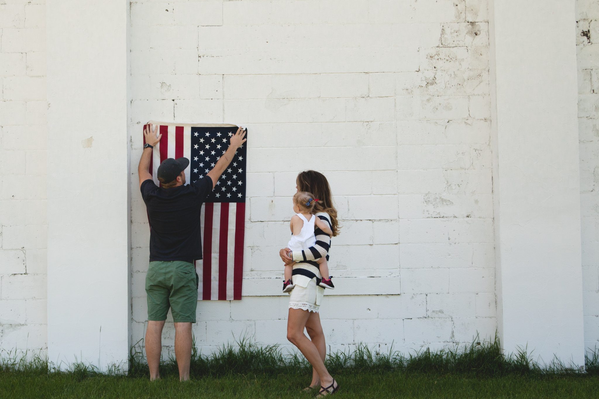 Photo of woman holding baby while man puts up American flag on building