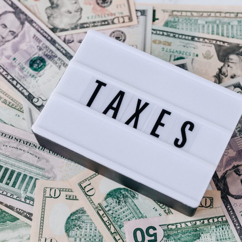The word "taxes" on a white background laid on top of several bills of US currency