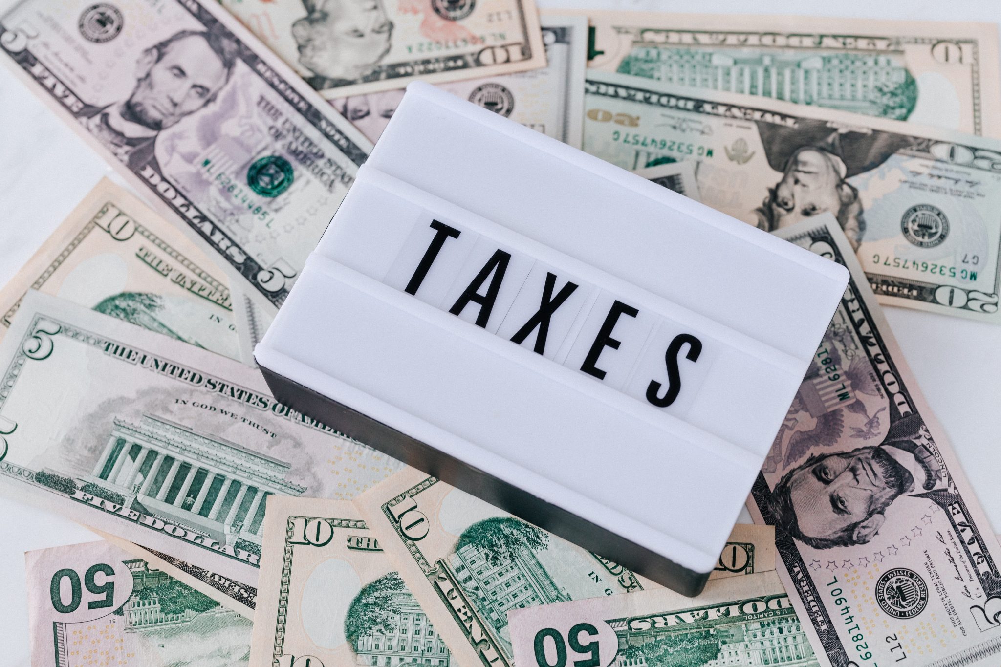 The word "taxes" on a white background laid on top of several bills of US currency