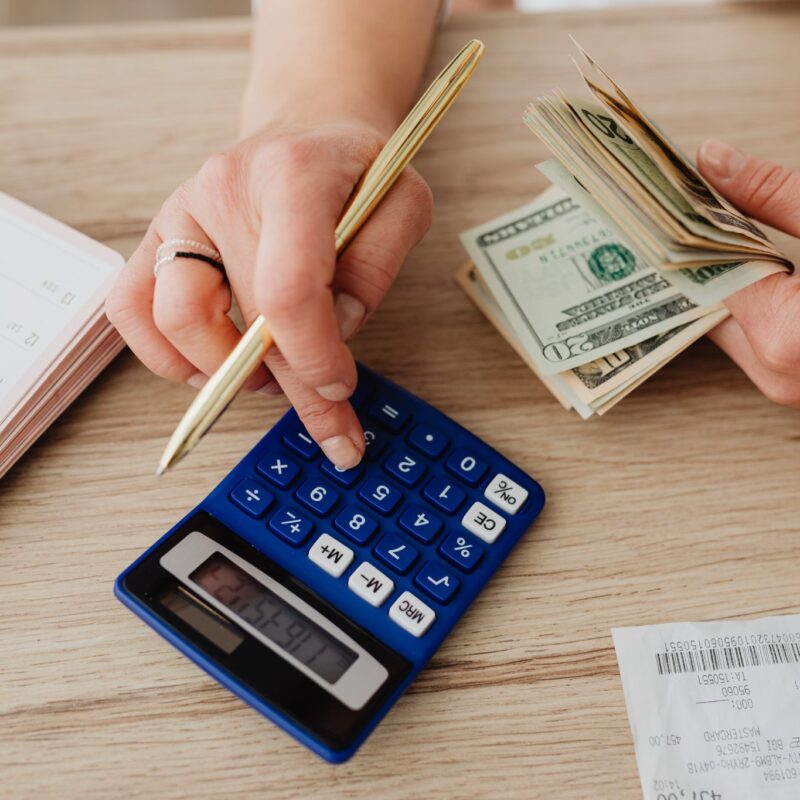 Person holding money in one hand, using a calculator with the other with receipts spread on a table.