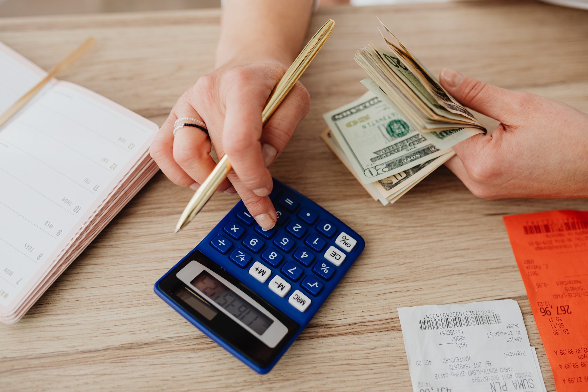 Person holding money in one hand, using a calculator with the other with receipts spread on a table.