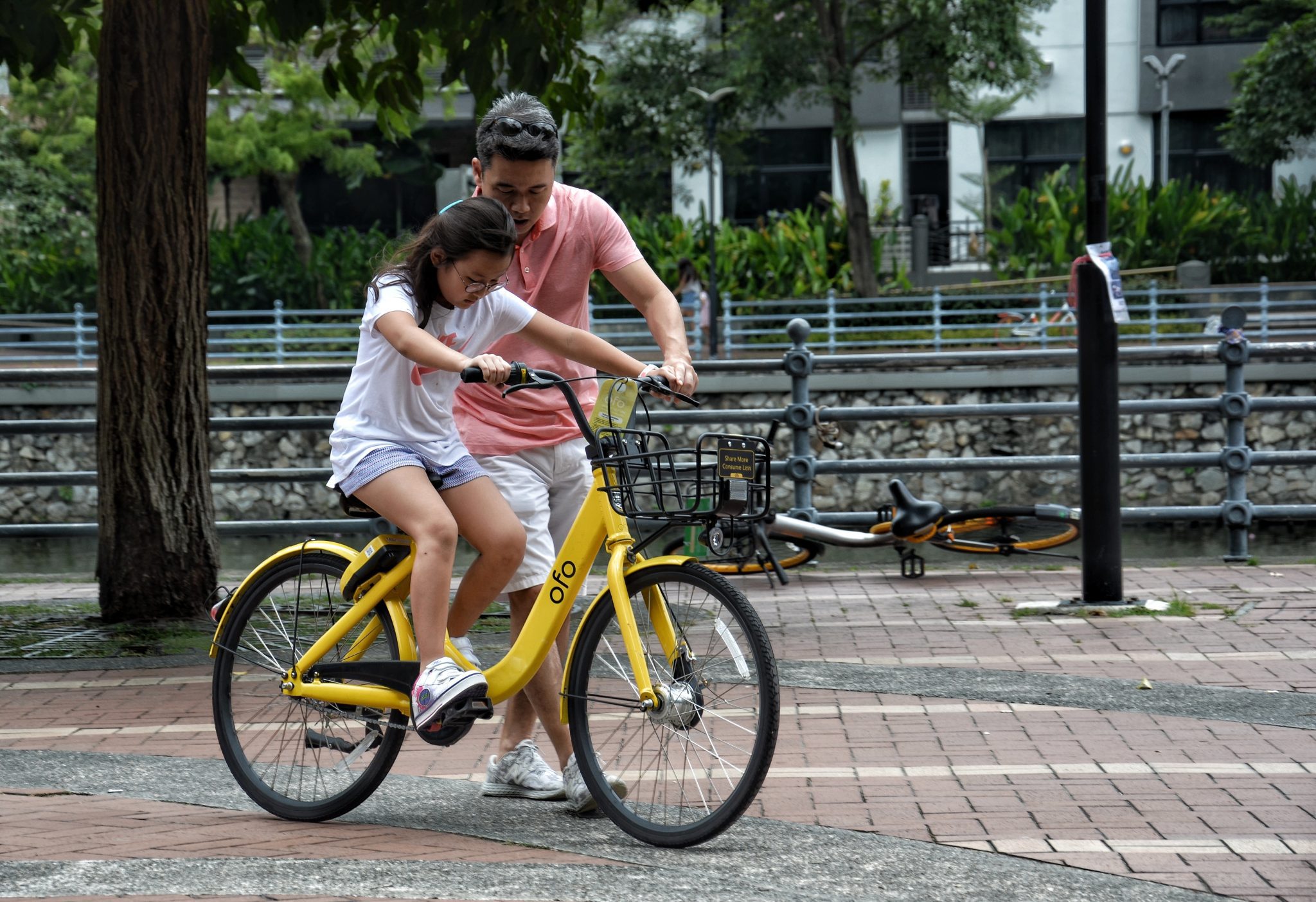 Girl riding bike beside dad as he helps guide her