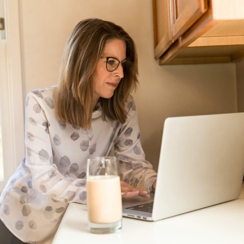 Woman leaning against counter typing on laptop