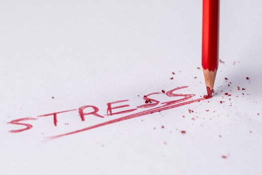 Red colored pencil writing the word STRESS