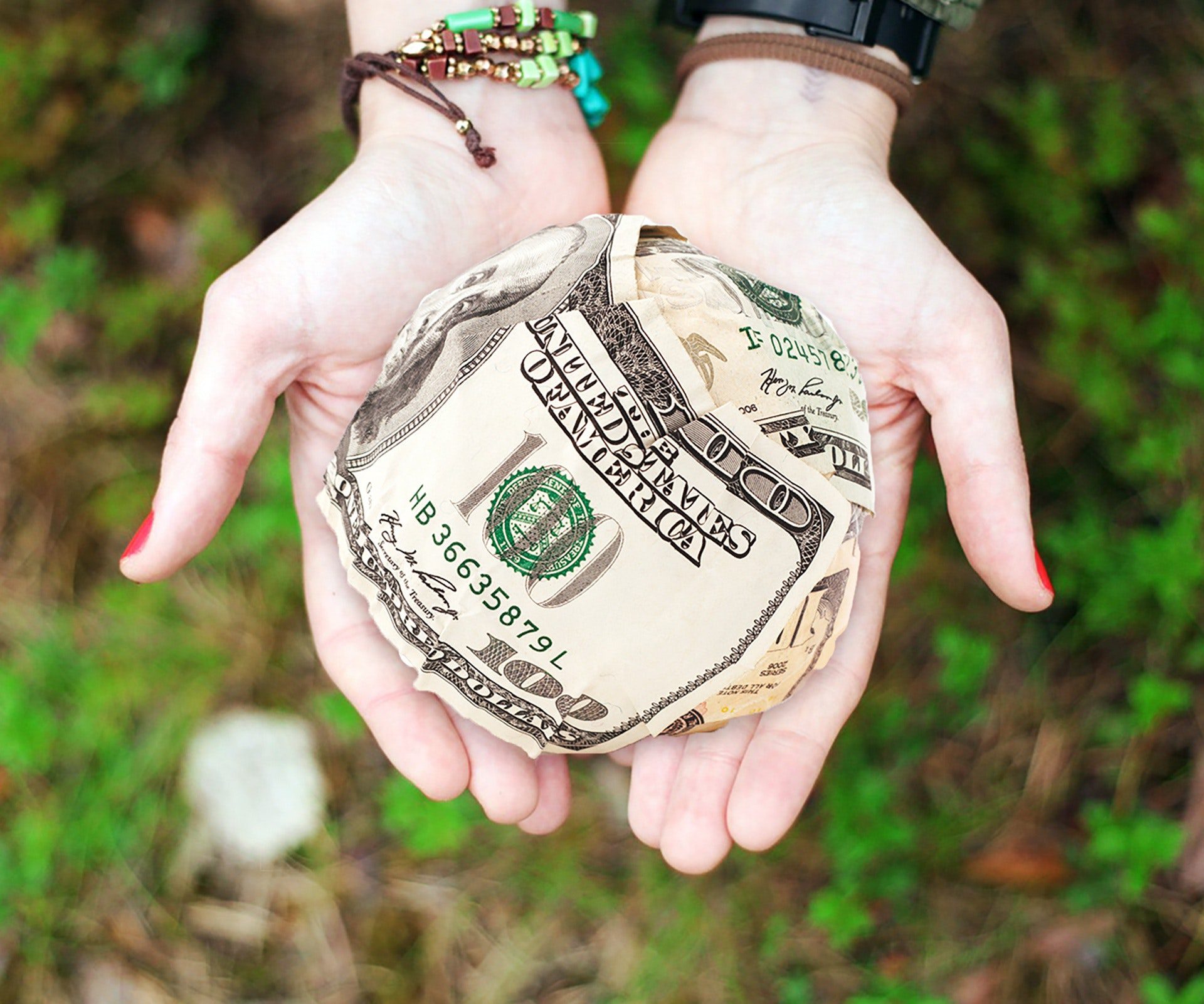 Two hands holding a ball of money with a 100 dollar bill visible