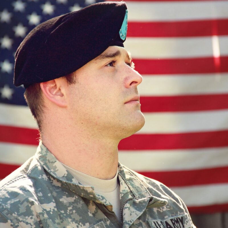 Man in Army uniform looking at American flag.