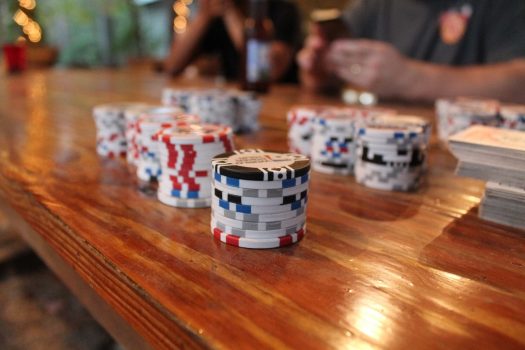 Photograph of colorful poker chips on a wooden table with people playing a card game in the background