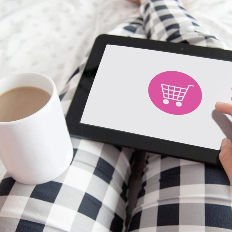Person holding coffee and a tablet with a grocery cart icon displayed