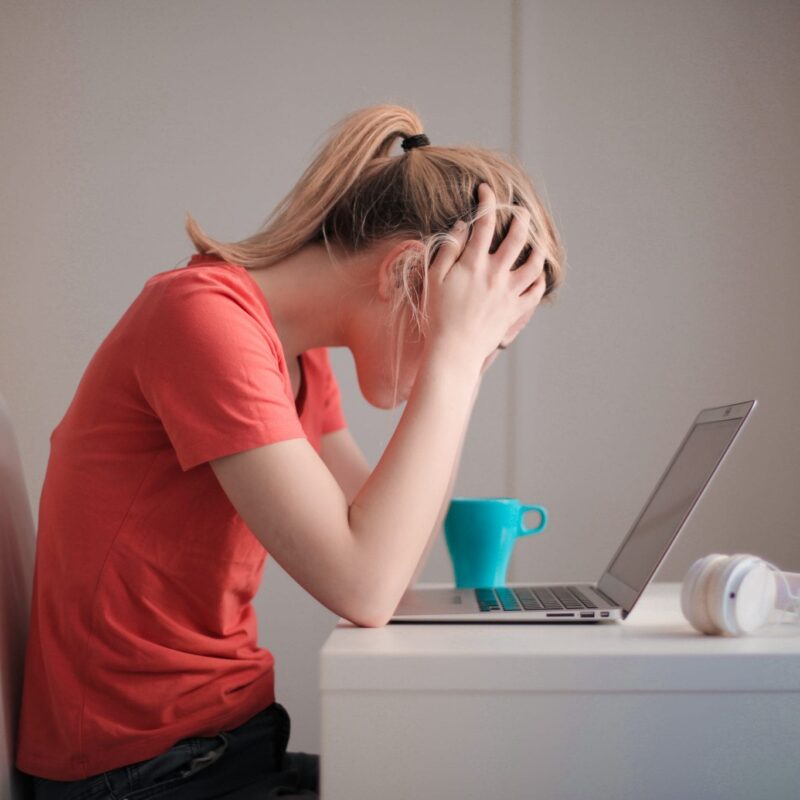 Woman holding her head and sitting in front of laptop