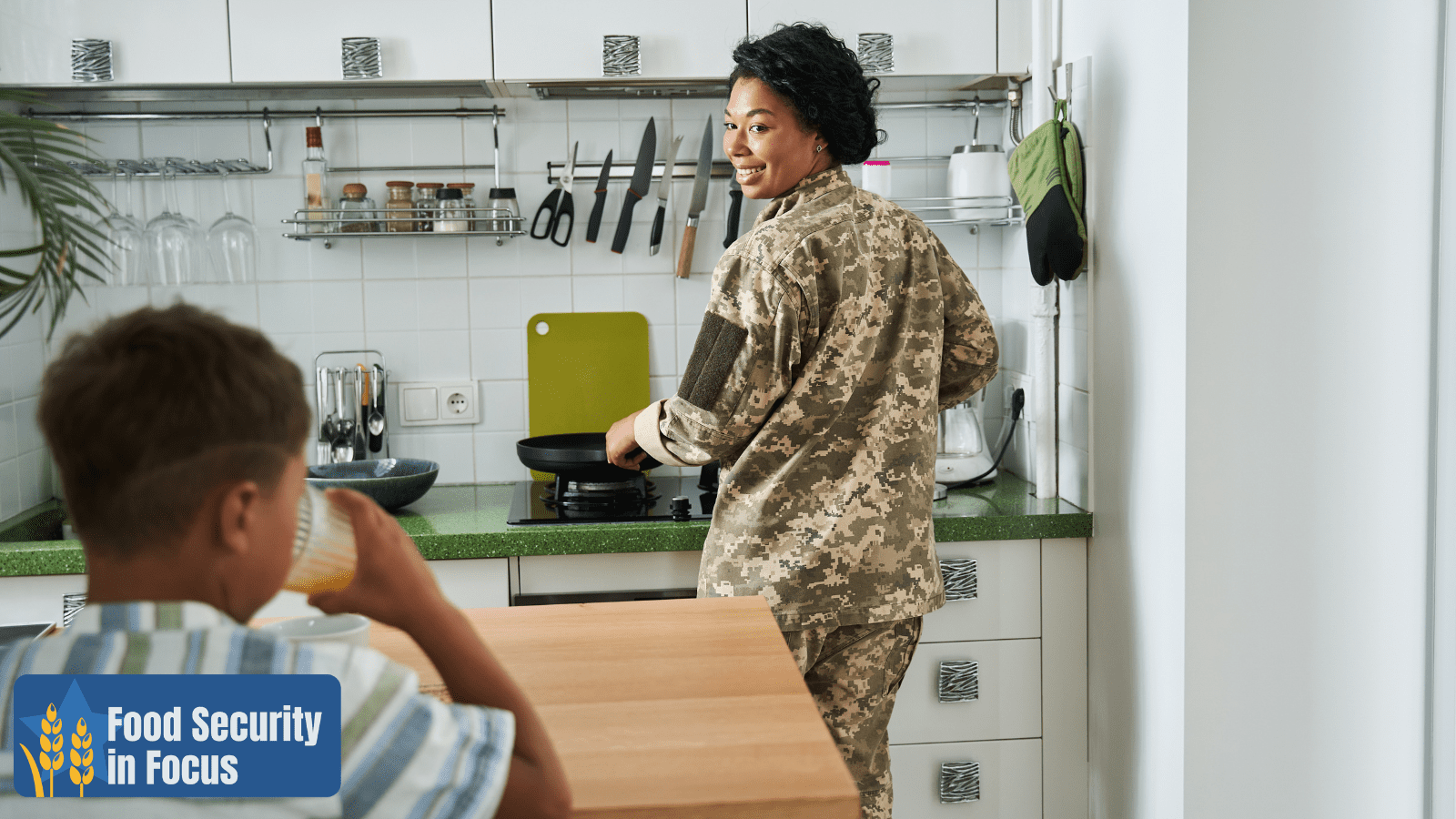 A woman in her uniform cooks breakfast for a young child in a kitchen, food security in focus logo