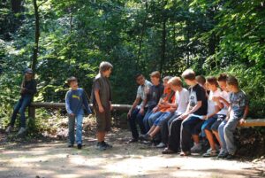 Group of pre-teen's sitting talking and laughing on a tree trunk across a trail.