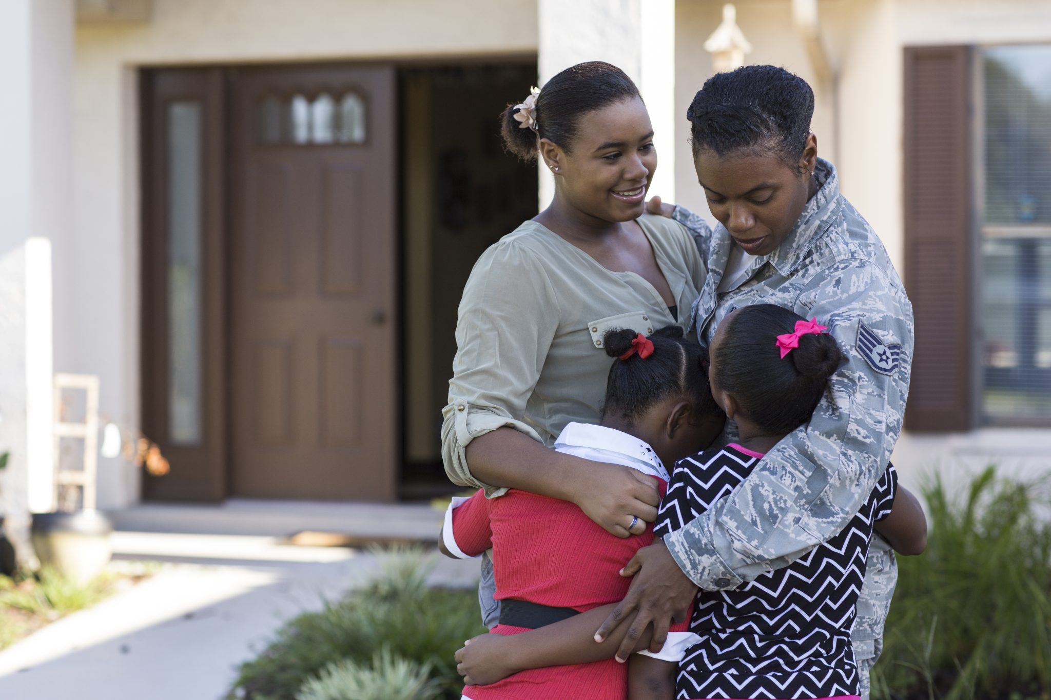 military family standing in front of a home hugging