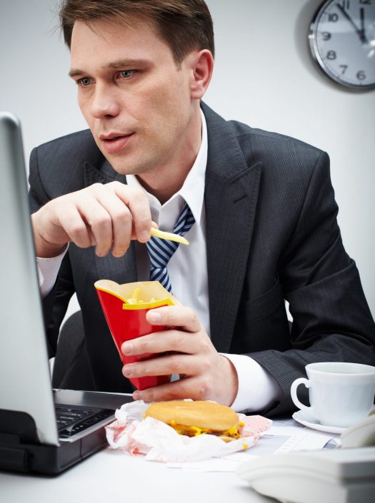 Man looking at laptop while eating burger and fries