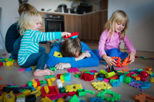 kids play with toys scattered all over and tired exhausted father