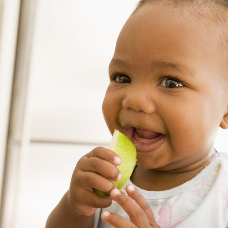 Happy black toddler girl eating apple indoors